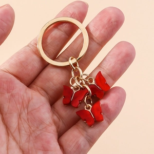 Detail of red acrylic butterfly keychain with gold clasp held in hand on pink background