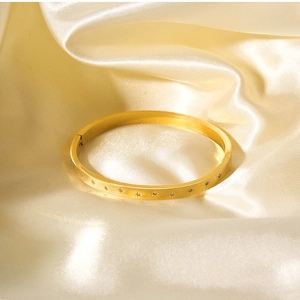 Dettaglio di un bracciale in acciaio dorato 18 carati con incisioni a stella su seta crema