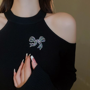 Detail shot of a bow brooch with sparkling purple and green zircons on a black sweater