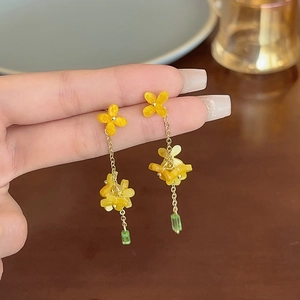 Macro detail of sweet yellow flower earrings with green drop bead and golden chain