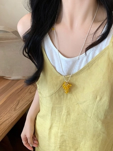 Dettaglio della collana con uva di perle di vetro gialle indossata da modella su legno