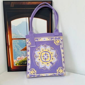 Purple knit tote bag with yellow mandala pattern on a clean white surface