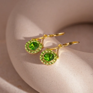 Close-up of vintage gold emerald earrings with light green diamonds on a warm display
