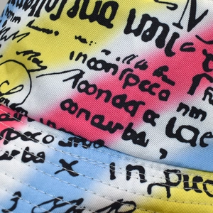Detail of colorful gradient bucket hat featuring black street style graffiti lettering