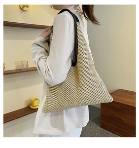 Detailed view of woven straw shoulder bag with black leather straps and mesh texture