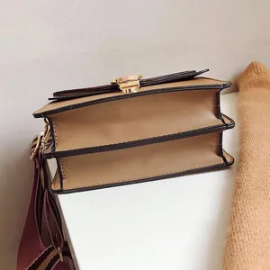 Detail of tan accordion crossbody bag with gold buckle and striped fabric strap