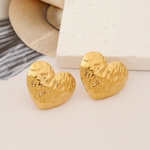 Detailed shot of golden irregular heart earrings with textured hammered finish on a stone pedestal