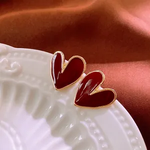 Elegant red heart enamel stud earrings with gold plating on a vintage ceramic plate