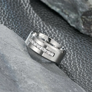 Close-up detail of a brushed titanium steel ring with a row of inlaid square zircons.