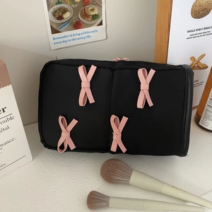 Detail of black fabric makeup bag featuring pink bows and cosmetic brushes on a desk