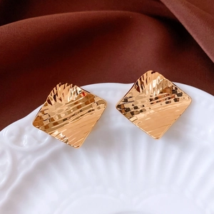 Close-up of square 18k gold earrings featuring a unique hammered water ripple texture