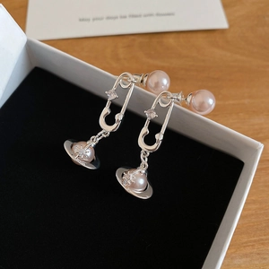 Détail d'une boucle d'oreille Saturne avec perle rose et design trombone sur boîte