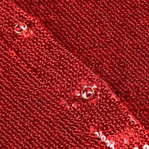 Macro shot of red high-density sequins and a faceted ruby-style jewel button on fabric