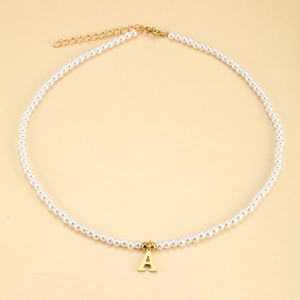 Detail of white pearl necklace featuring a polished gold letter A pendant and lobster clasp