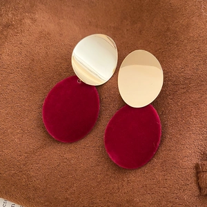 Détail de boucles d'oreilles ovales en velours rouge et métal doré sur tissu foncé