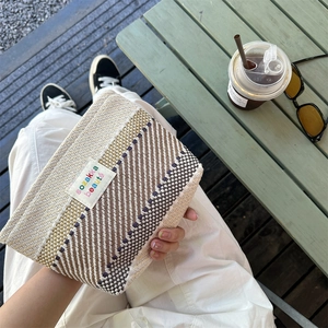 Detail of woven cosmetic bag texture with embroidered logo on cream striped fabric