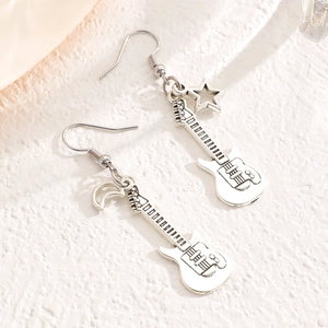 Dettaglio di orecchini vintage a forma di chitarra d'argento con ciondoli stella e luna