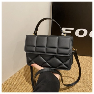 Detailed shot of black quilted faux leather handbag with gold hardware and top handle