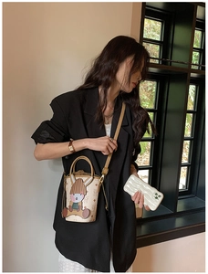 Detail of crossbody bucket bag with rabbit charm and classic monogram pattern on a model