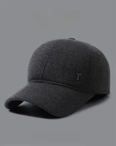 Close-up of dark grey textured baseball cap featuring metal letter T and ear flaps