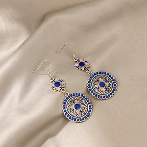 Detailed macro view of Bohemian floral enamel earrings on a champagne silk background