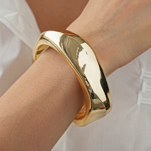 Close-up of a chunky irregular golden metal bangle with a polished liquid-style finish