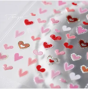 Macro detail of 3D heart nail art stickers featuring red plaid and glitter textures