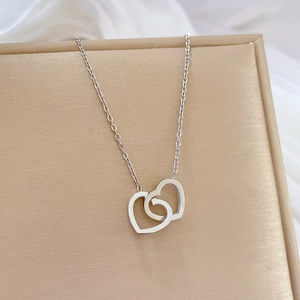 Close-up of silver interlocking heart necklace on a beige textured jewelry display box