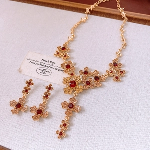 Macro detail of luxury gold flower necklace and red gemstone earrings on beige fabric