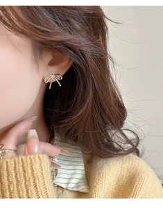 Close-up of minimalist silver bow earrings and matching ring on model's ear and hand
