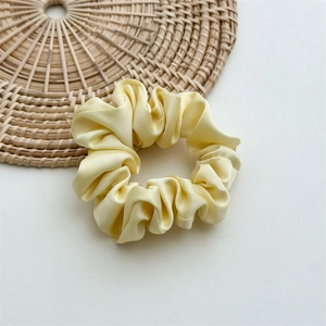 Detailed view of yellow satin scrunchie fabric texture on a minimalist background