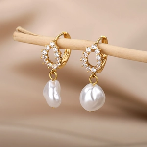 Close-up of golden pearl earrings with zircons hanging on a decorative wooden branch