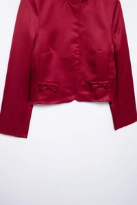 Detail of red satin blouse with round neck and elegant bow decorations on the hemline