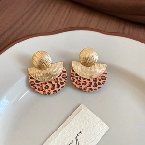 Détail de boucles d'oreilles rétro avec motif léopard et texture dorée dans un bol en céramique