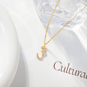 Macro shot of gold letter J pendant with a zircon floral detail on a white surface