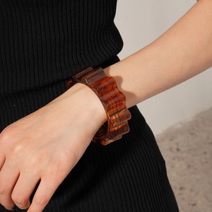 Macro detail of amber resin bangle featuring a wide wavy texture on a model's wrist