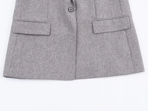 Detail of grey herringbone blazer showing single black button and symmetrical flap pockets