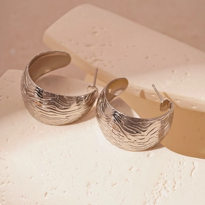Détail macro de boucles d'oreilles géométriques en C argentées à texture ondulée fluide