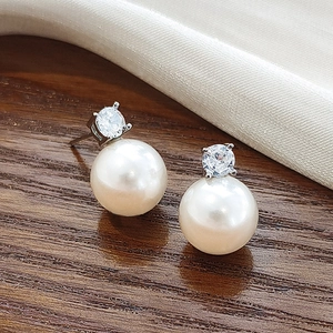Macro shot of silver pearl earrings with sparkling cubic zirconia on a wooden base