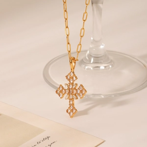 Détail du collier pendentif croix doré serti de zircons sur un fond beige chaleureux