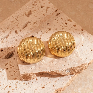 Boucles d'oreilles créoles dorées à texture ondulée sur fond en pierre naturelle