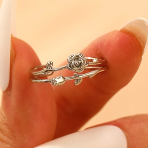 Detailed view of silver rose and leaf open ring worn on a finger with white nail polish