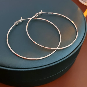 Close-up of silver hoop earrings with a hammered texture on a green jewelry box