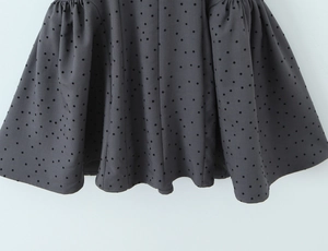 Detailed view of the black flocked polka dot pattern and hemline stitching on a grey dress