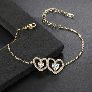 Detail of gold bracelet showing intertwined zircon hearts and lobster clasp on dark base