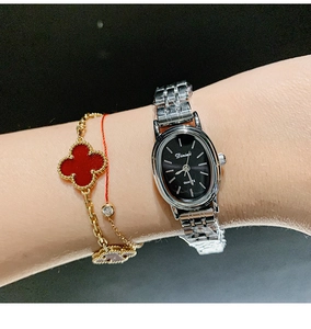 Close-up of a silver metal strap watch with oval black dial worn with a red bracelet