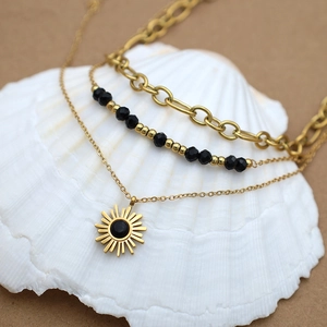 Detailed close-up of triple-layered gold sun pendant necklace with black beads on seashells