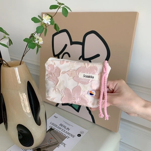 Detail of pink floral textured cosmetic bag with cord zipper pull and brand tag