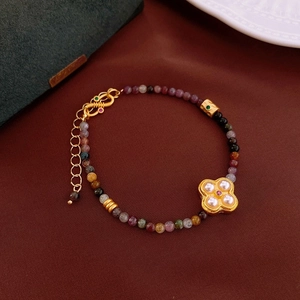 Detail of colorful tourmaline beaded bracelet with a gold clover pearl pendant on red fabric