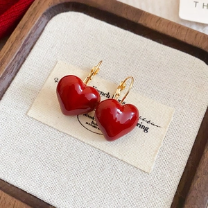 Detail of red enamel heart-shaped earrings with gold hooks on a beige textured fabric